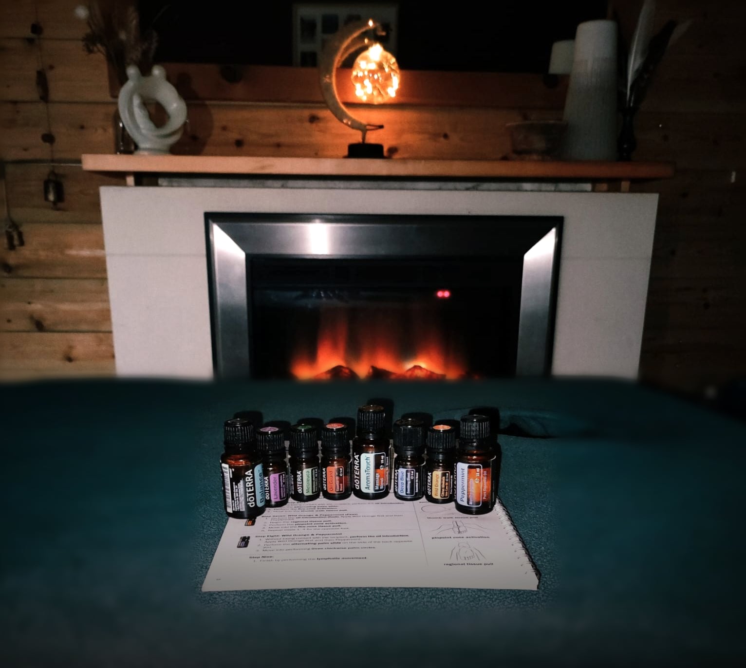 The AromaTouch ritual space: a warmed treatment table set with eight essential oils, softly lit by a fireplace
