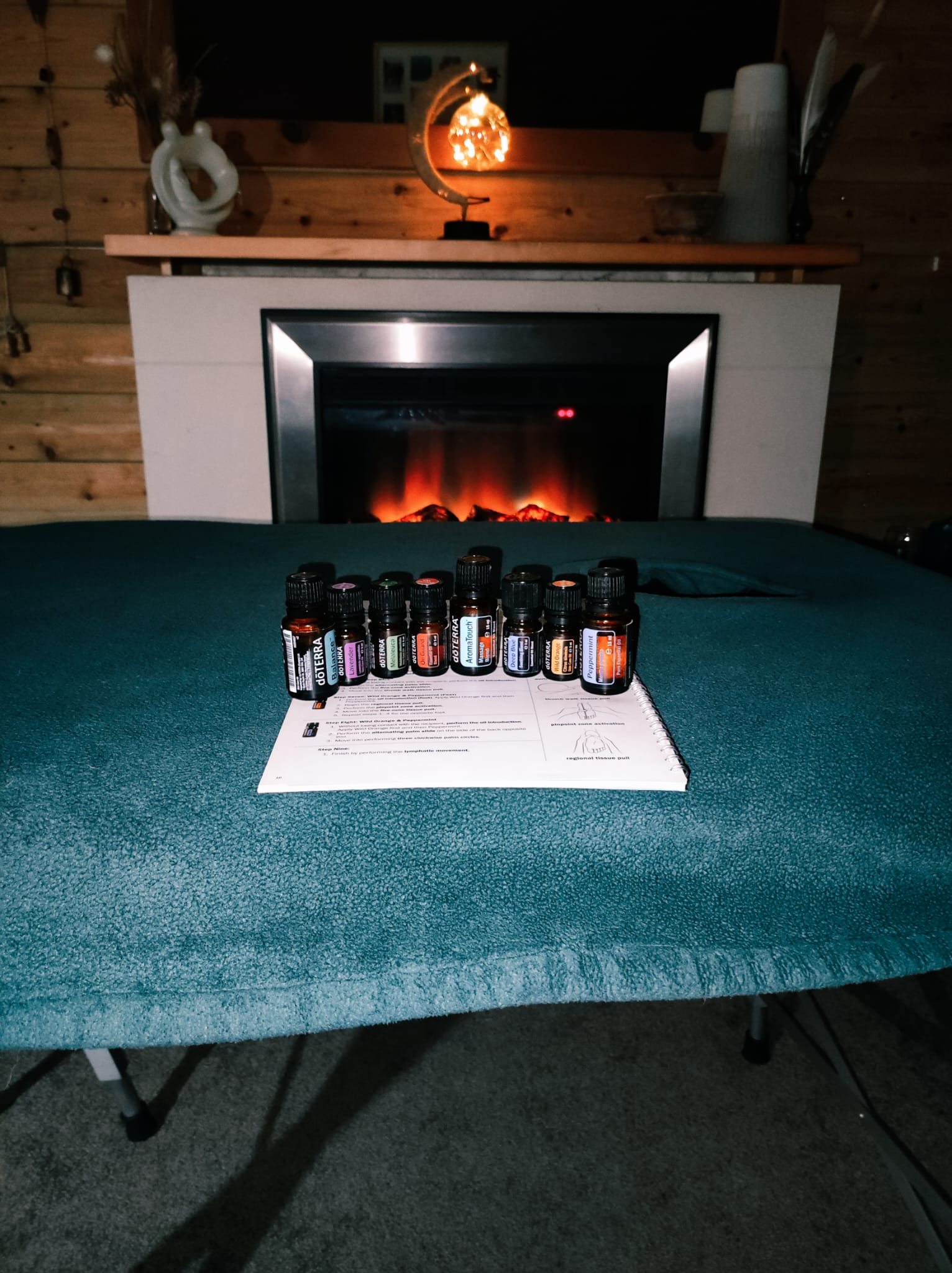 The AromaTouch ritual space: a warmed treatment table set with eight essential oils, softly lit by a fireplace